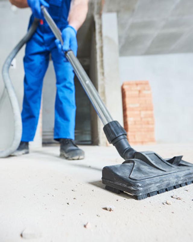 persona apsirando el piso de un sitio acabado de construir con escombros restantes de el proceso de construcción